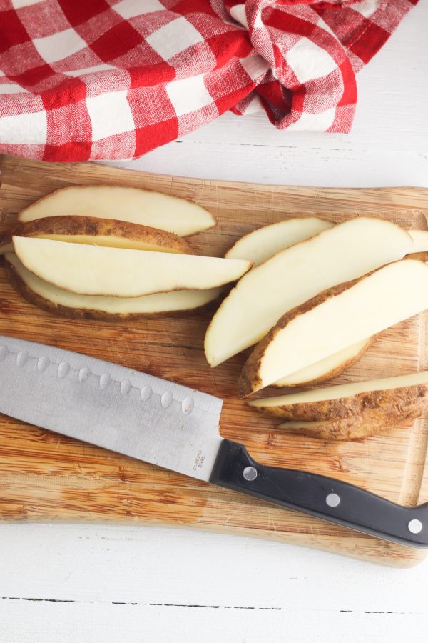 freshly sliced potato wedges on a cutting board next to a chef's knife