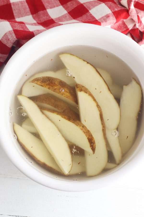 sliced potato wedges in water in a white bowl