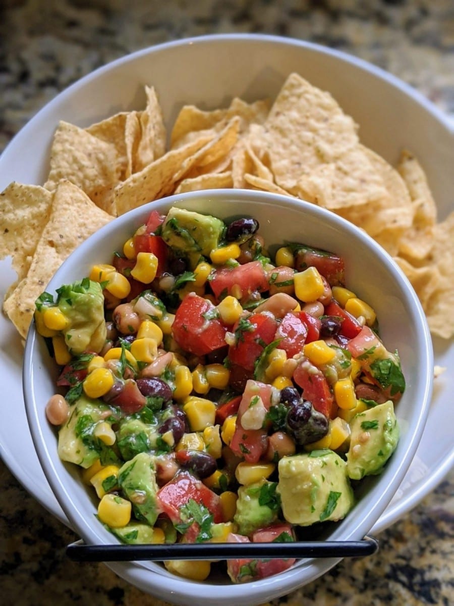 Finished avocado and black bean salad in a white bowl with chips