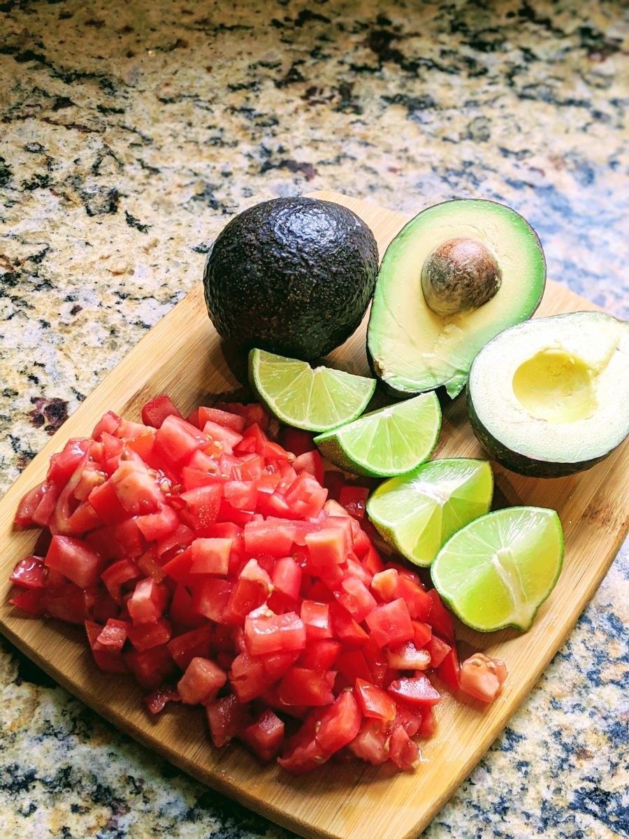 Cutting board with cut tomatoes, sliced limes, and sliced avocados