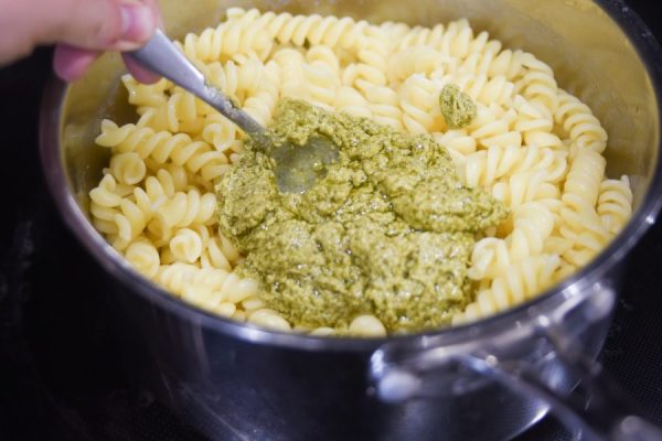 cooked pasta with pesto being mixed in