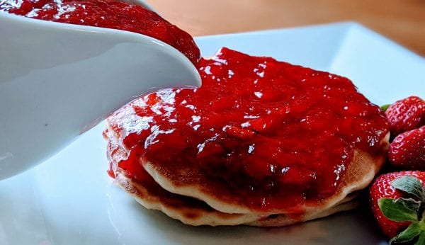 pouring strawberry syrup on pancakes